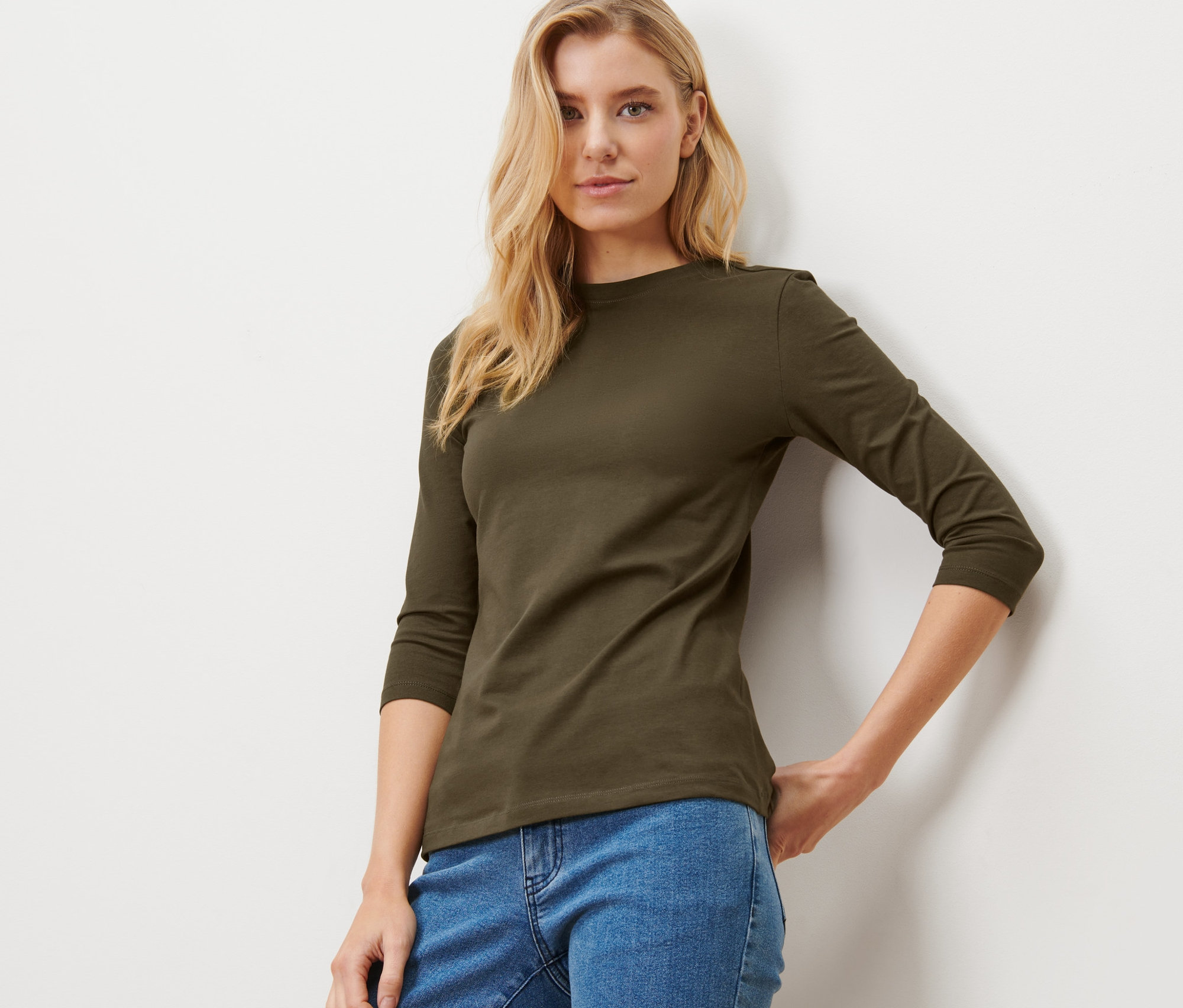 Blonde Frau posiert in einem khaki Shirt mit 3/4-Arm.