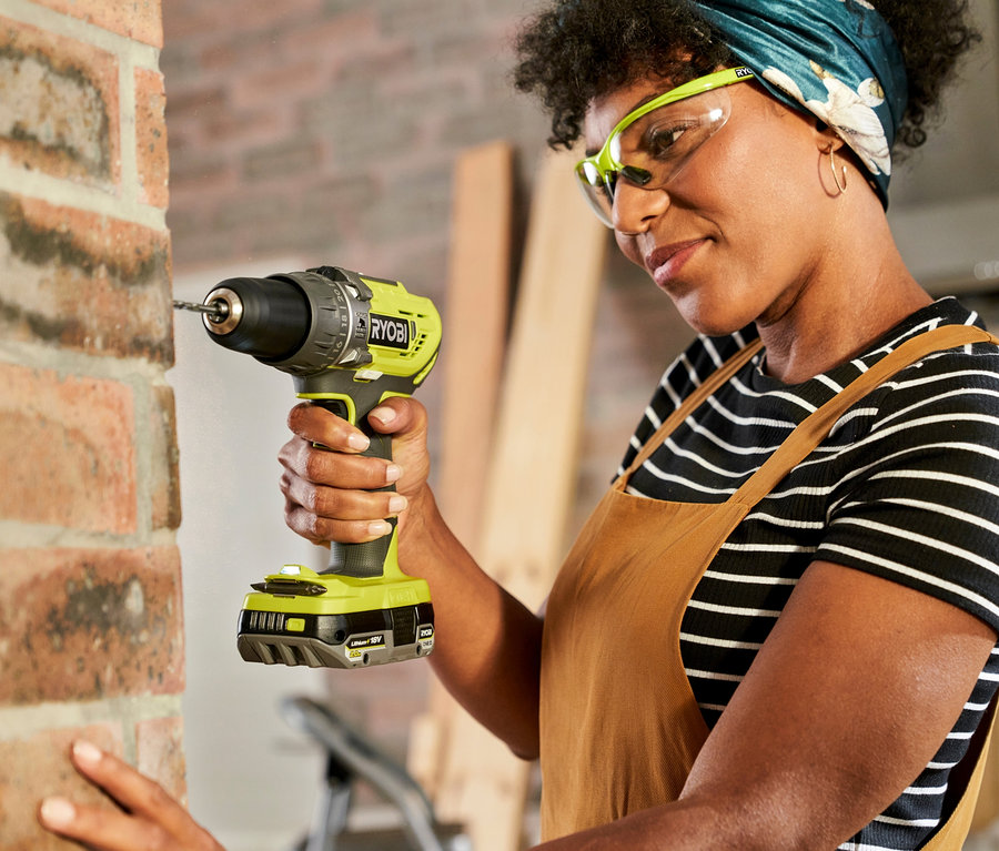 Frau bohrt mit dem RYOBI 18 V ONE+ Heimwerker-Set »R18PD3-220TAH« in eine Ziegelwand.
