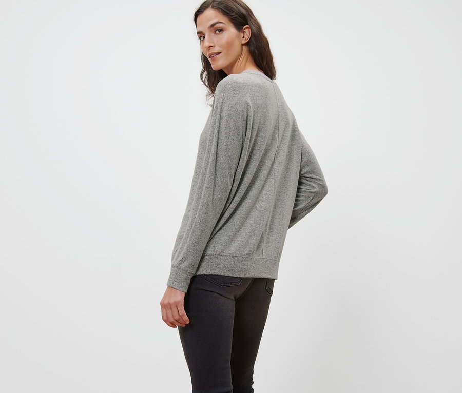 Frau blickt über die Schulter und trägt ein graues Fledermausshirt und schwarze Jeans.