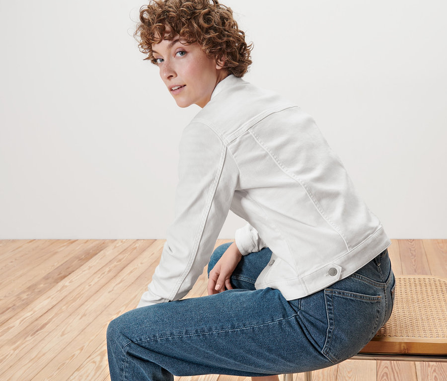 Frau sitzt auf einem Stuhl und trägt eine weiße Jeansjacke.