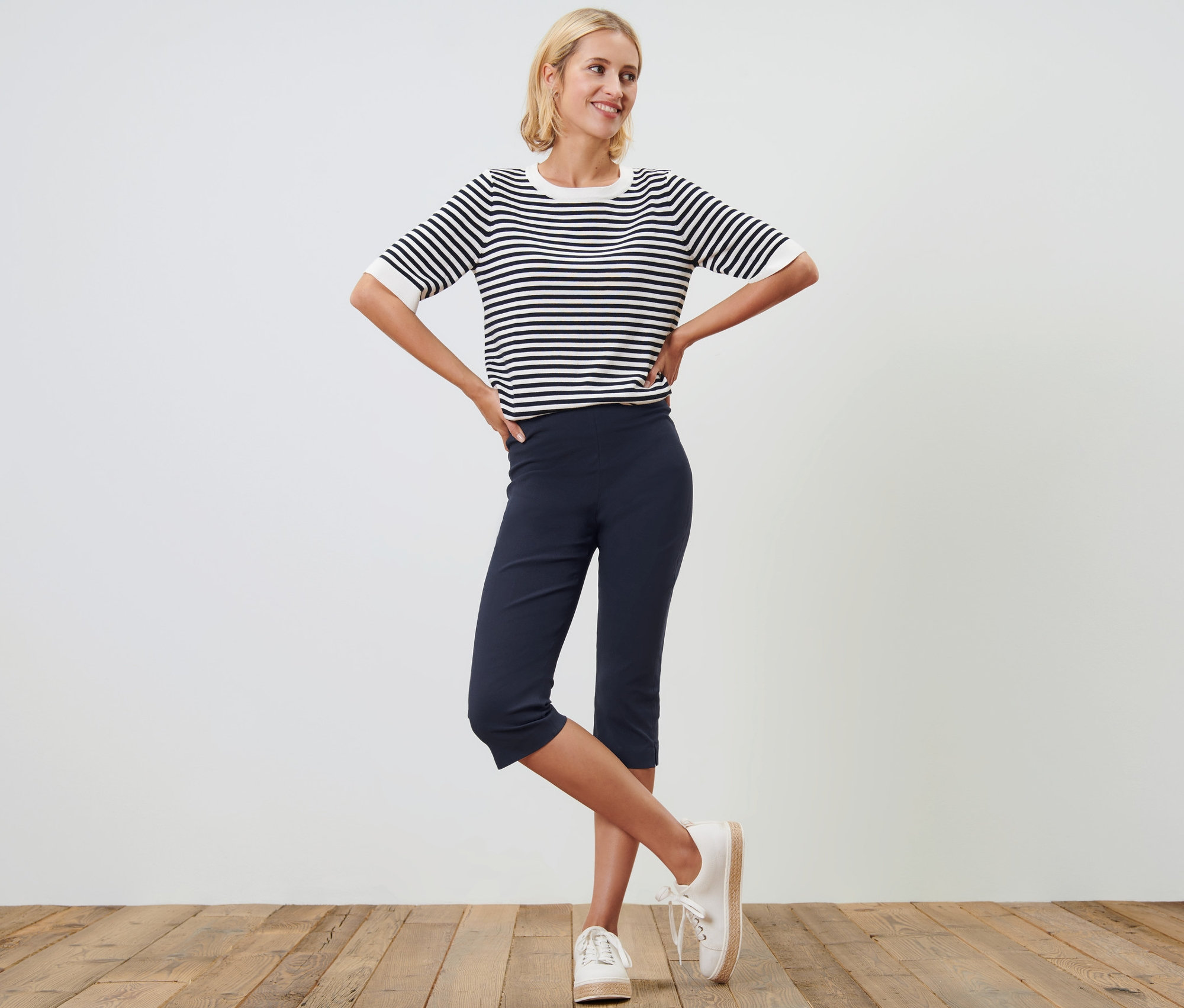 Frau posiert in dunkelblauer 3/4-Stretchhose und einem gestreiften Oberteil.