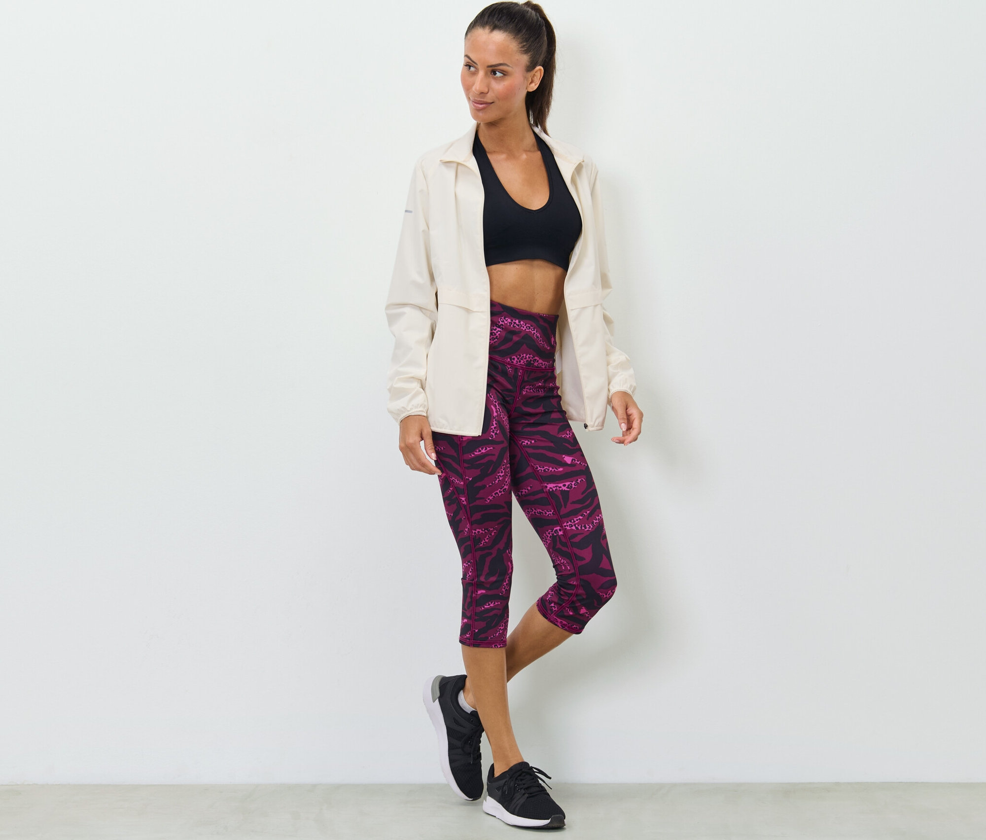 Frau posiert in Sport-BH, Jacke und 3/4-Sporttight mit Alloverprint.