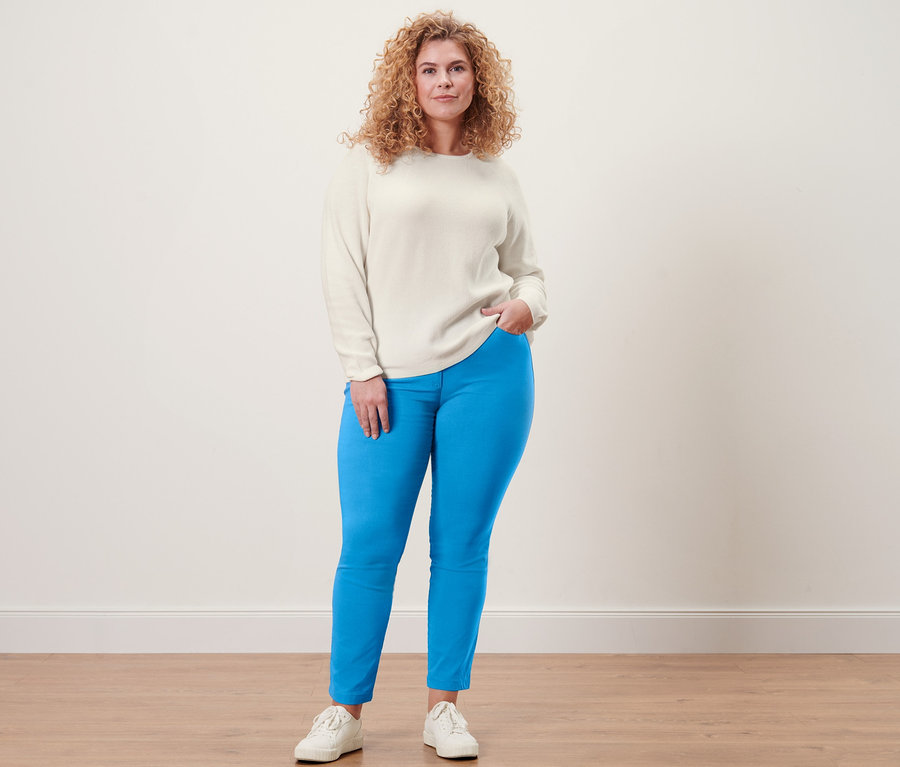 Frau posiert in cremeweißem Strickpullover und Bengalin-Hose.