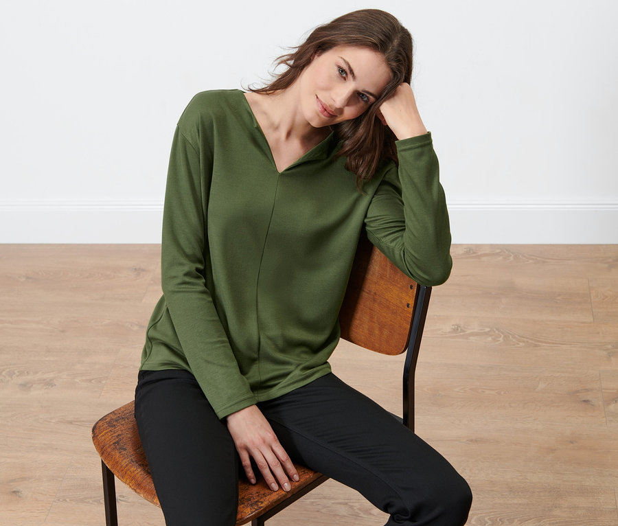 Frau sitzt auf einem Stuhl und trägt ein Blusenshirt.