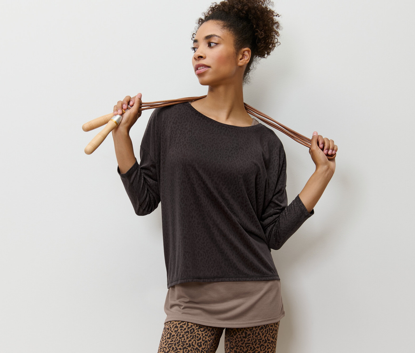 Frau posiert mit braunem 2-in-1-Sportshirt und Springseil.