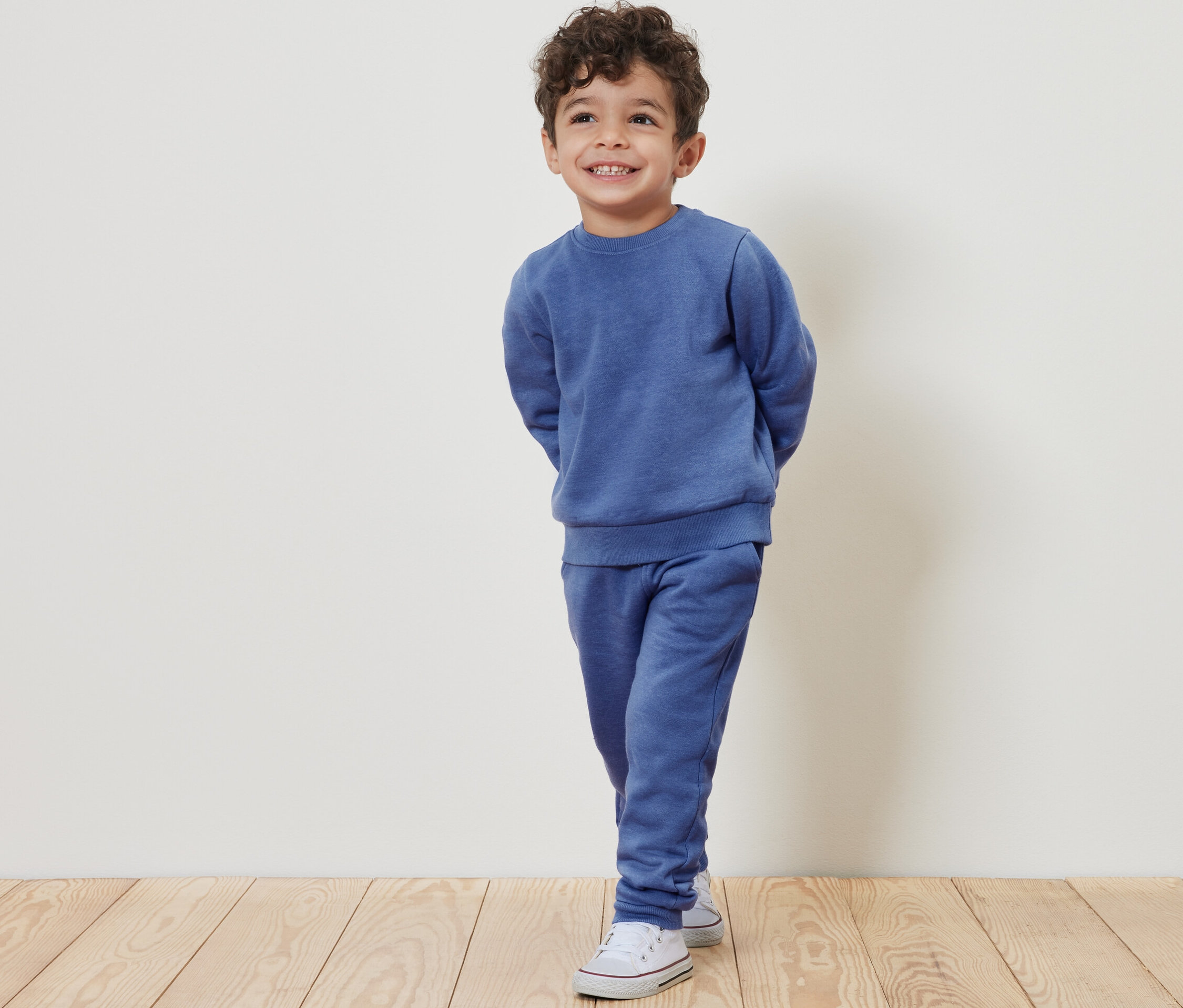 Ein lächelnder Junge posiert in einem hellblauen Trainingsanzug und weißen Turnschuhen.