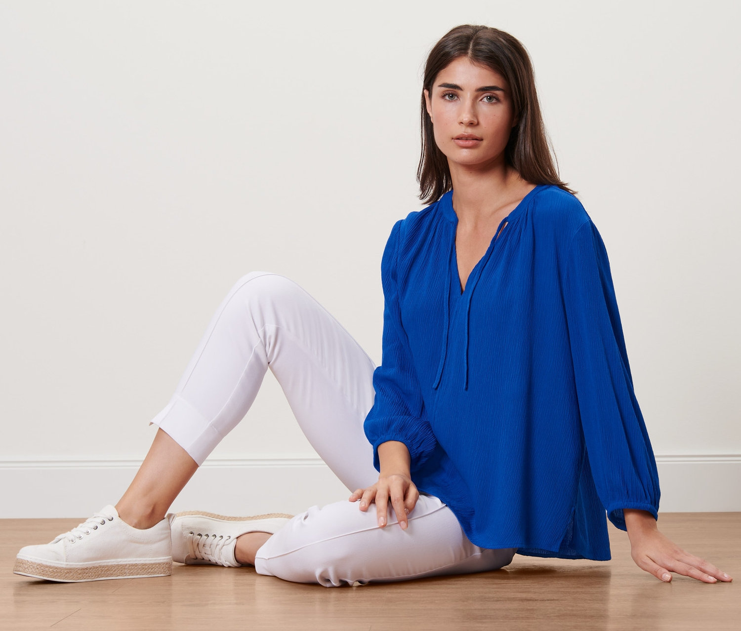 Frau sitzt auf dem Boden und trägt eine blaue Tunika-Bluse.