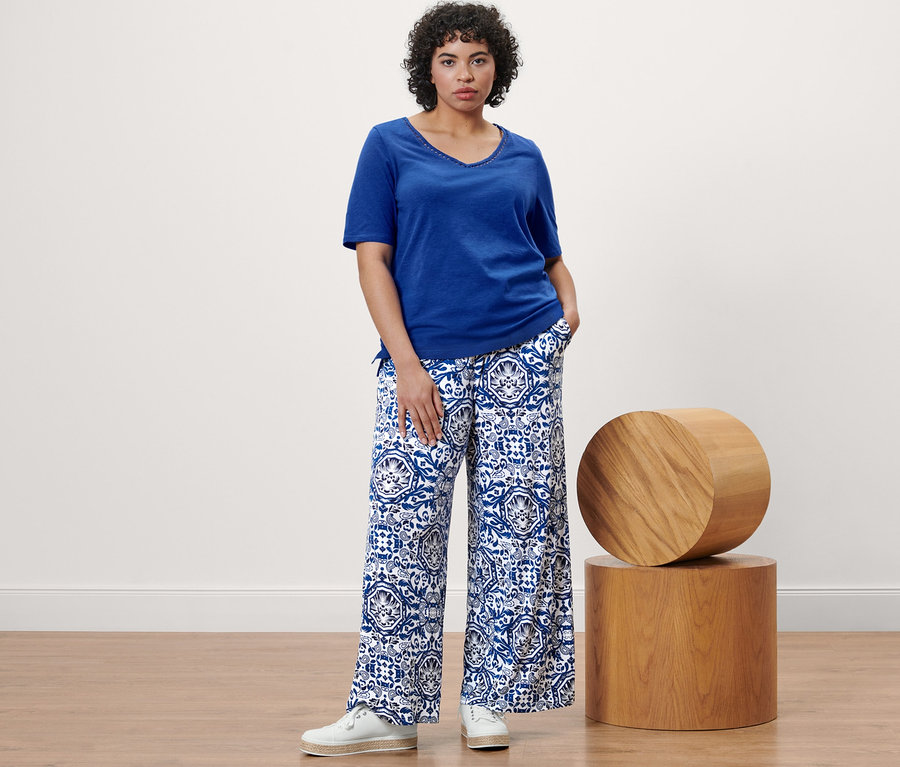 Frau posiert in kobaltblauem Shirt und bedruckter Palazzohose.