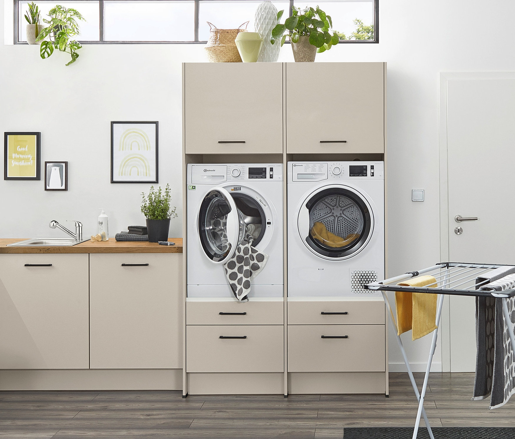 Einrichtung eines Waschraums mit Waschmaschine mit offener Tür, Trockner und einem Modulschrank für Waschmaschine und Trockner in Kieselgrau.