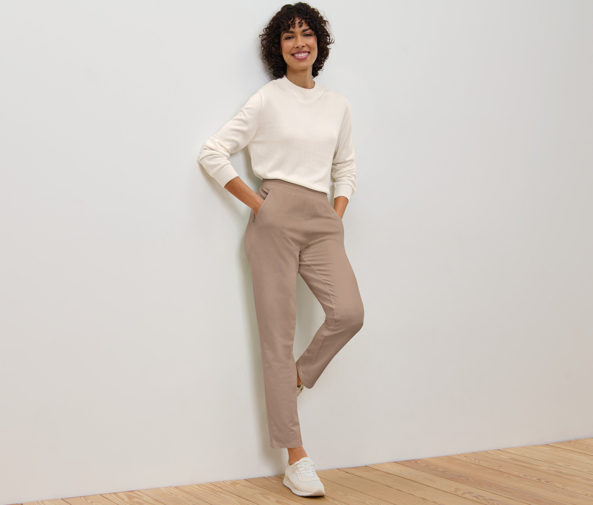 Frau lehnt an Wand und posiert in beigen Joggpants.