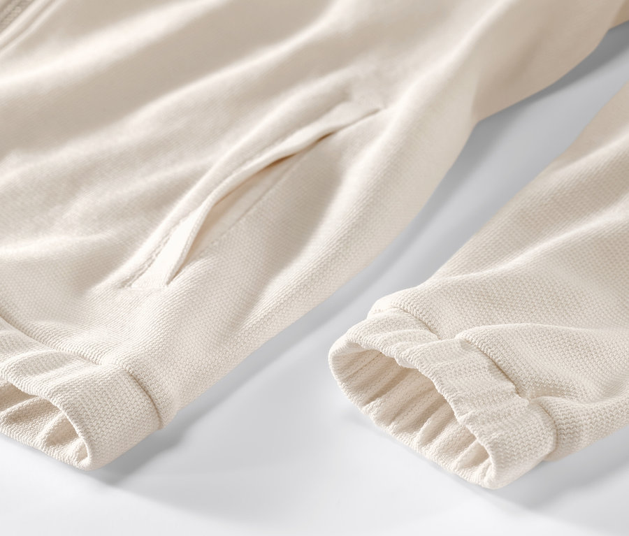 Detailansicht einer cremeweißen Sweatjacke mit Reißverschluss und Tasche.