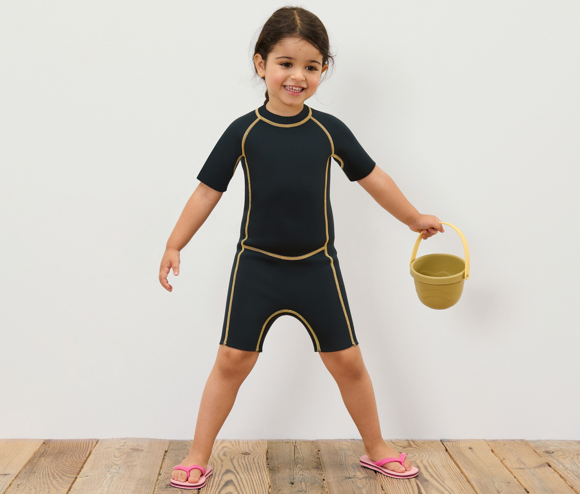 Mädchen im Kinder-Neoprenanzug hält gelben Eimer.