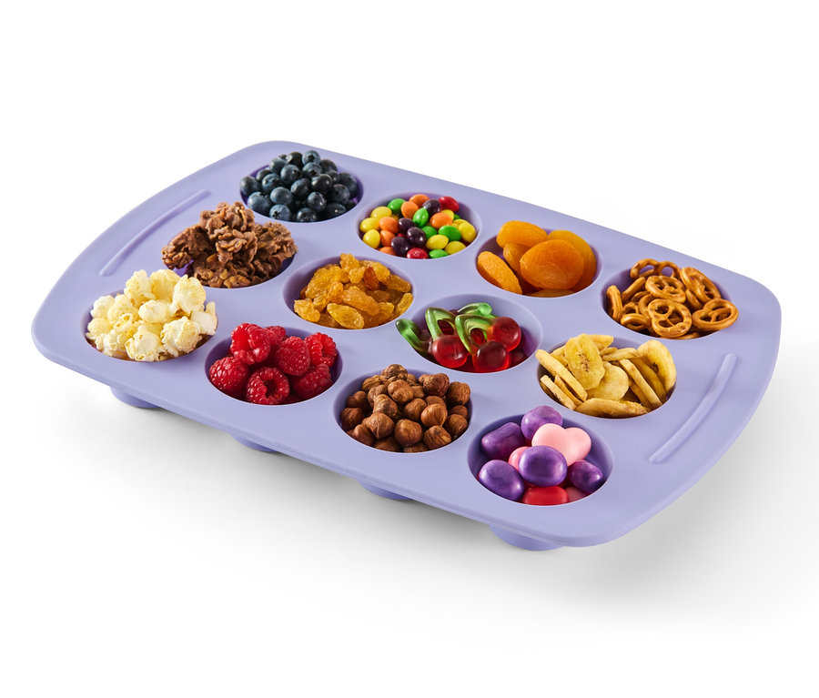 Lila farbenes, faltbares Silikon-Muffinblech gefüllt mit Blaubeeren, Frühstücksflocken, Schokolinsen, Aprikosen, Brezeln, Popcorn, Himbeeren, Nüssen, Kirschen, Bananenchips und Süßigkeiten.