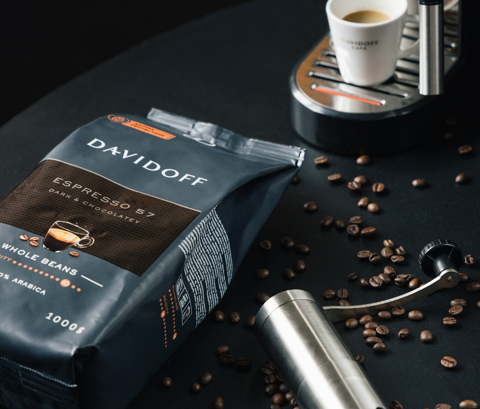 Eine Packung DAVIDOFF CAFÉ Espresso 57 - 1x 1000 g Ganze Bohne, eine Kaffeemühle und eine Espressotasse unter einer Kaffeemaschine.
