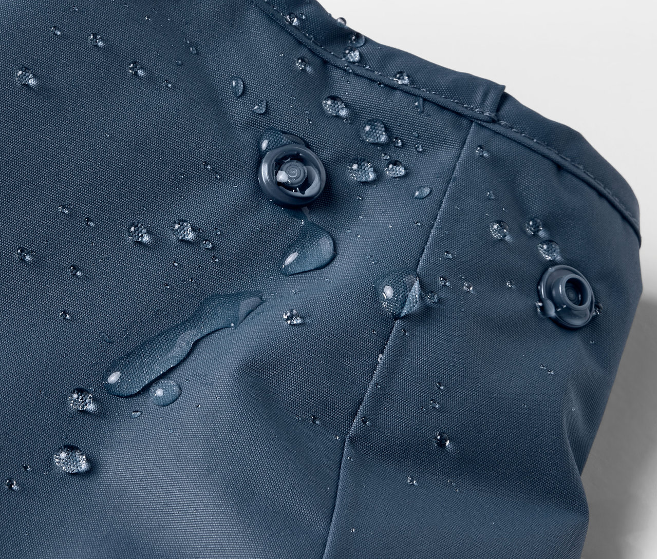 Detailaufnahme einer blauen Kinder-Thermo-Regenhose mit Wassertropfen und Druckknöpfen.