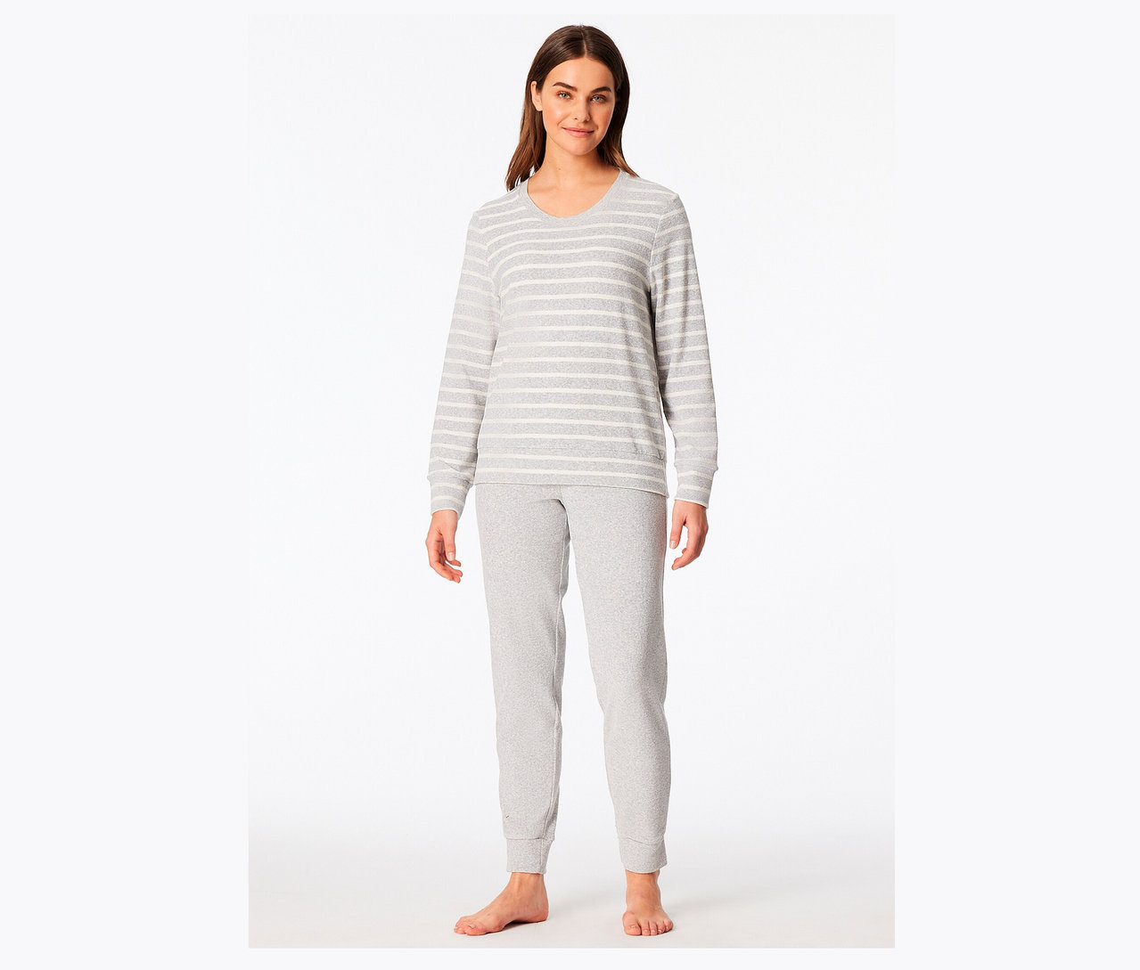 Frau steht barfuß und trägt einen grau-weiß gestreiften Pyjama.