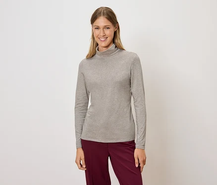 Frau posiert in einem grauen Rollkragenpullover und weinroten Hosen.