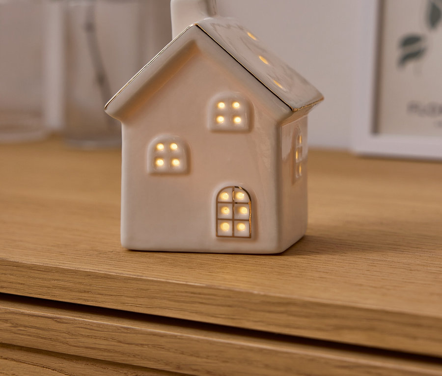 Dekorative Keramikhaus-Leuchte mit beleuchteten Fenstern steht auf einer Holzkommode.