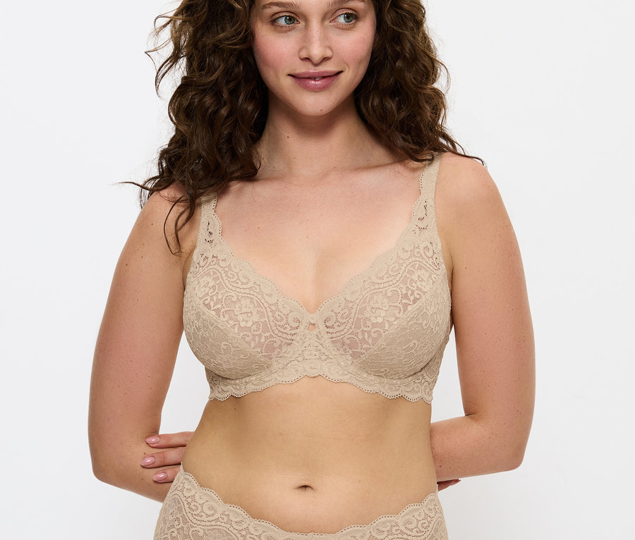 Frau mit braunen Haaren posiert in einem beigen Spitzen-BH und Höschen.