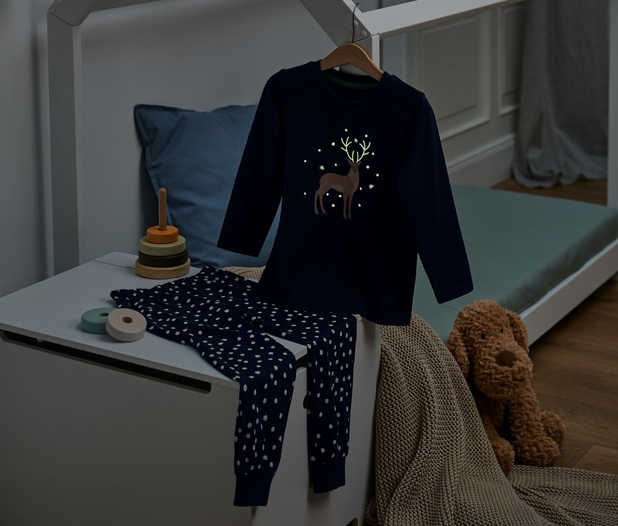 Dunkelblauer Glow-in-the-dark-Pyjama mit Bio-Baumwolle mit Hirschmotiv auf einer Truhe im Kinderzimmer.