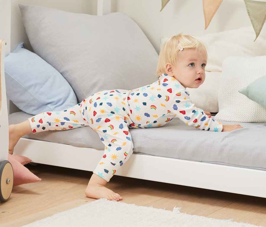 Kleinkind liegt auf dem Bauch auf einem Bett und trägt einen Schlafanzug aus Bio-Baumwolle (3 Stück).