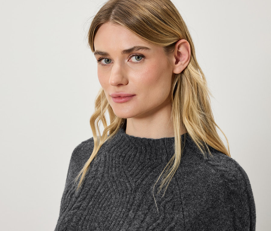 Porträt einer blonden Frau in einem grauen Strickpullover.