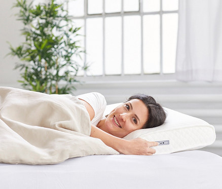 Frau liegt im Bett auf einem Medisana-SleepWell-Kissen »SP 100« mit Soundsystem und lächelt.