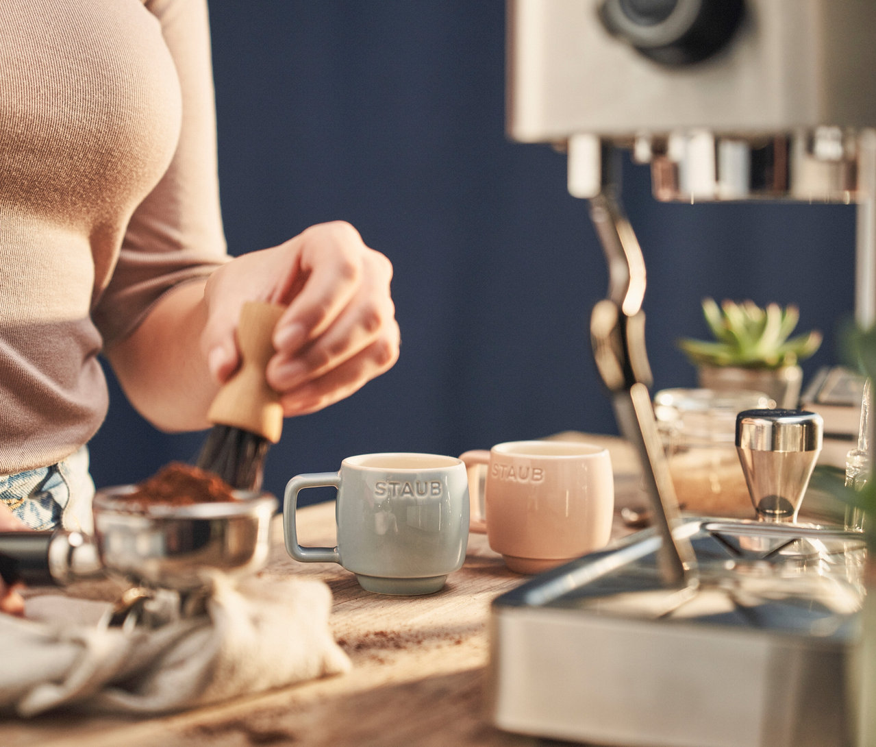 Frau reinigt Siebträger neben zwei STAUB Espressotassen »Macaron« auf einem Holztisch.
