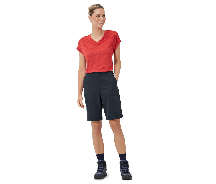 Frau steht in rotem Shirt und blauer 2-in-1-Funktionshose.