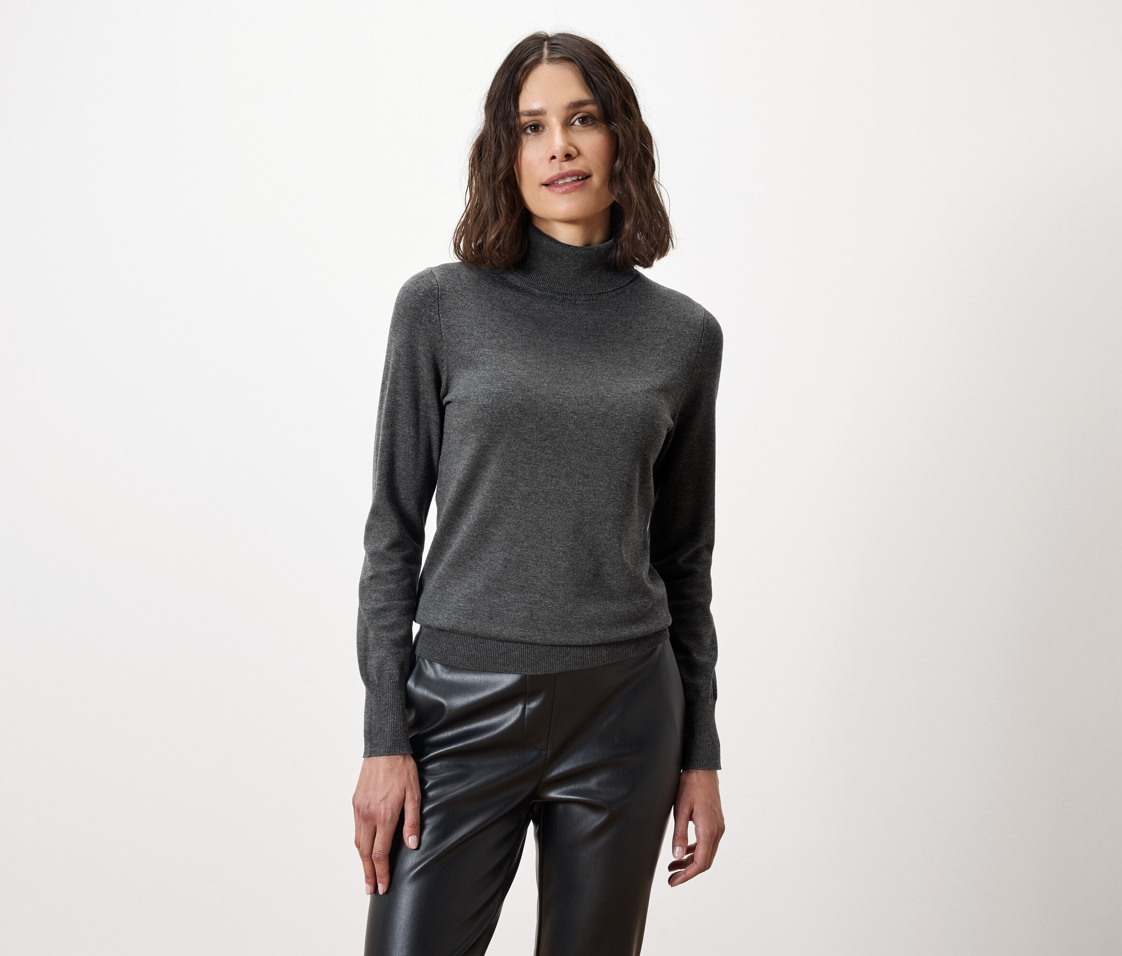 Frau posiert in einem grauen Rollkragenpullover und einer schwarzen Lederhose.