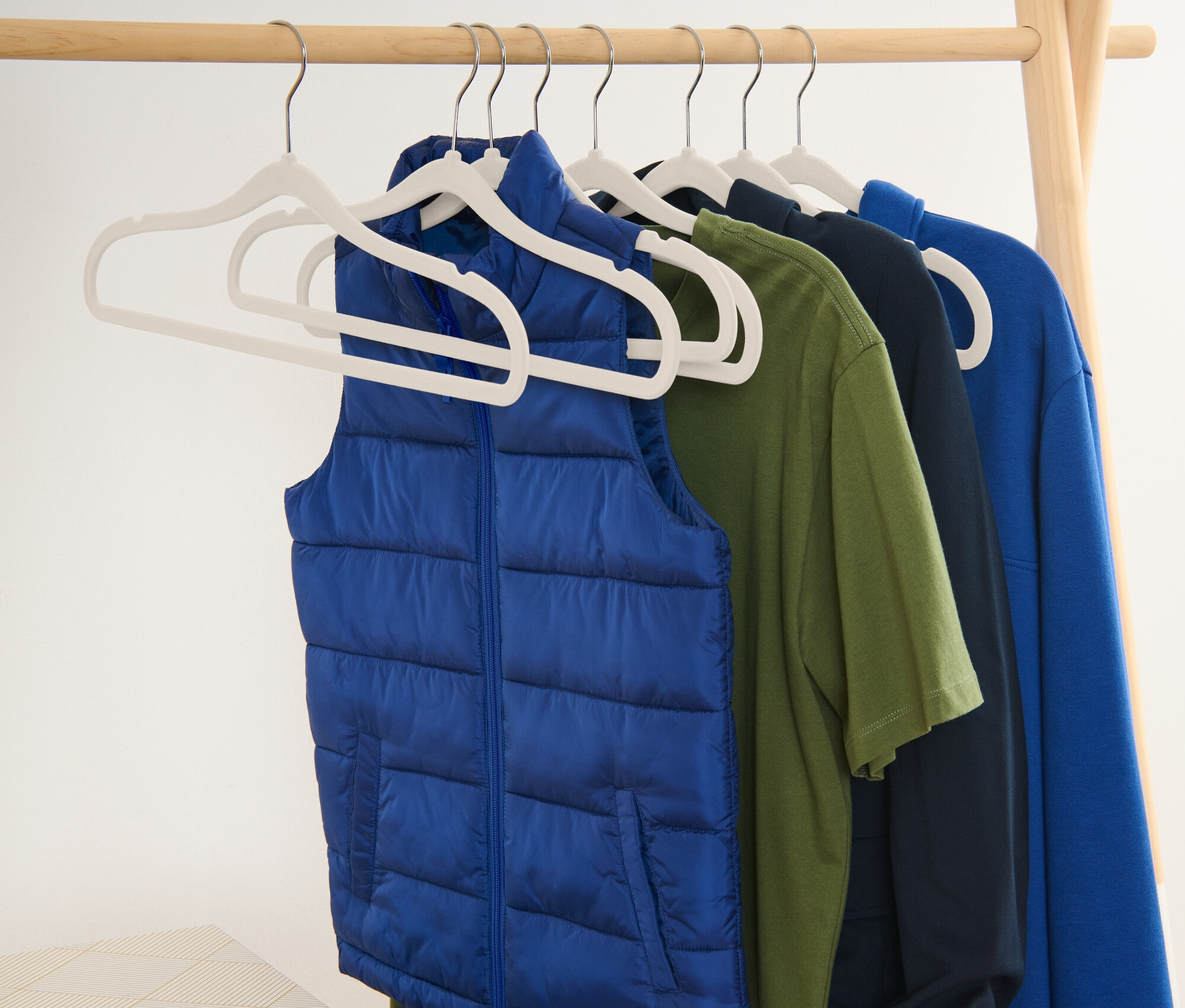 Blaue Weste und T-Shirts hängen an Kleiderbügeln an einem Holzständer.
