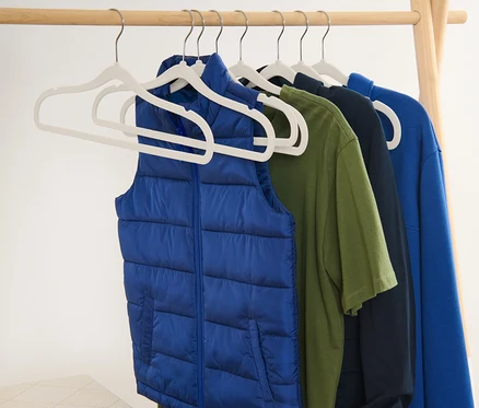 Blaue Weste und T-Shirts hängen an Kleiderbügeln an einem Holzständer.