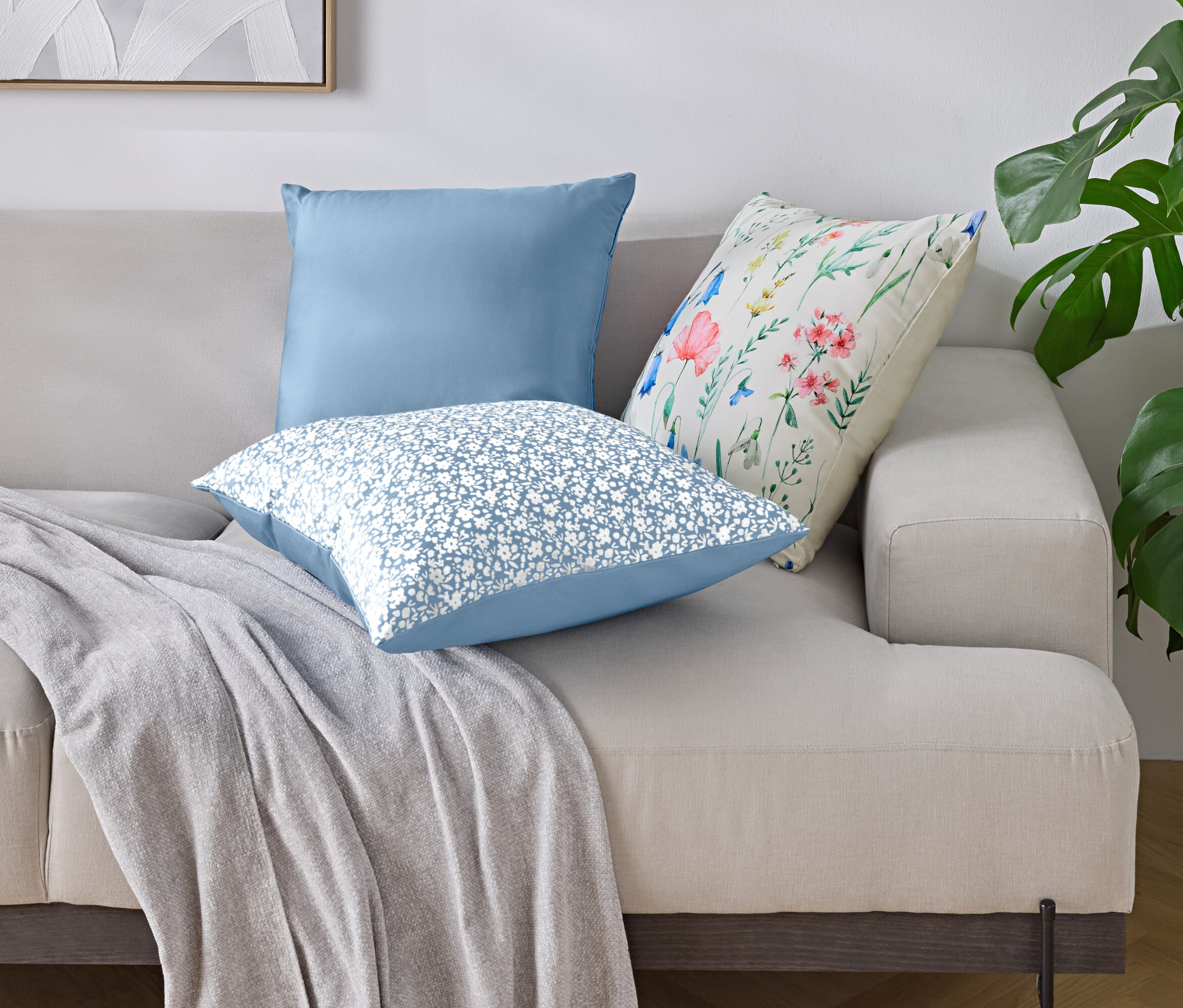 Auf einem Sofa liegen drei Kissen und eine Decke.