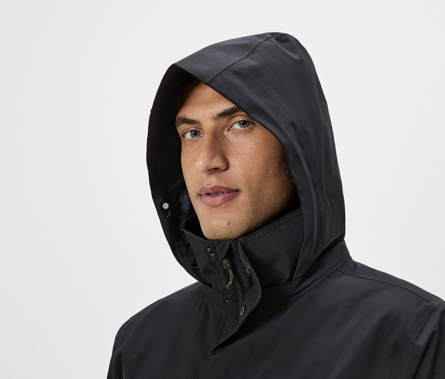 Porträt eines Mannes, der eine schwarze Kapuzenjacke vor einem hellen Hintergrund trägt.