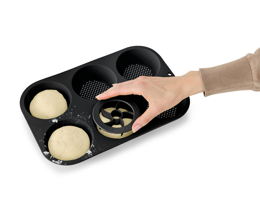 Hand drückt Ausstecher in Teig in schwarzer Muffinform.