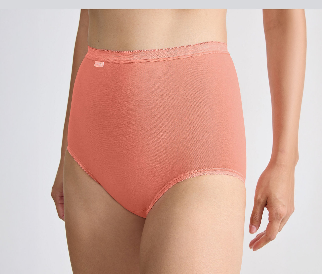 Eine Person trägt orangefarbene sloggi Basic+ Maxi C3P Maxi-Slips mit hohem Bund und geripptem Saum.