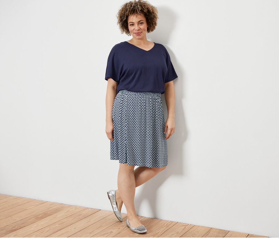 Frau posiert in dunkelblauem, strukturiertem Shirt und bedrucktem Jerseyrock.