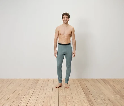 Ein Mann mit freiem Oberkörper steht auf einem Holzboden und trägt graue Leggings.