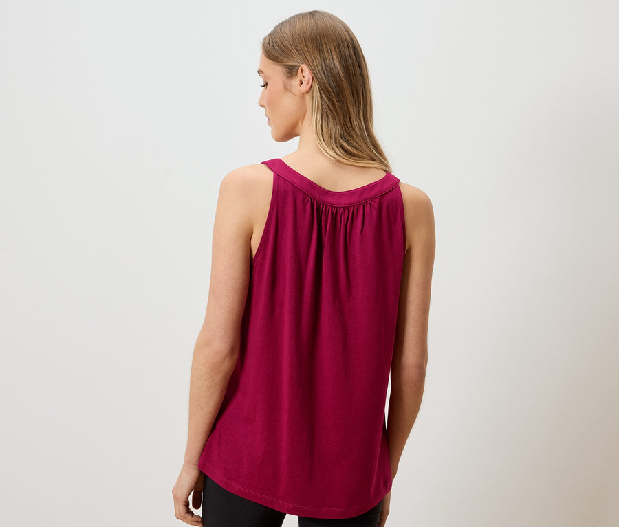 Rückansicht einer Frau mit langen blonden Haaren, die ein ärmelloses, weinrotes Oberteil und schwarze Leggings trägt.