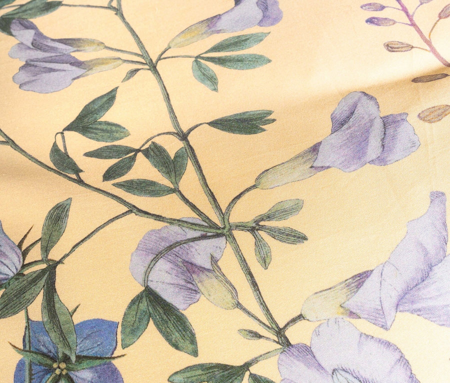 Nahaufnahme eines hellgelben Stoffes mit Blumenmuster in Lila- und Blautönen.