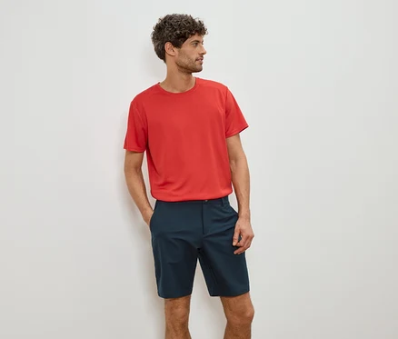 Mann mit rotem T-Shirt und blauen Shorts, die Hände in den Taschen.