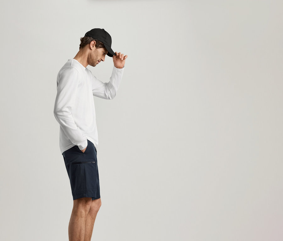 Mann mit schwarzer Kappe und marineblauen Shorts, der ein weißes 2 Langarmshirts trägt.