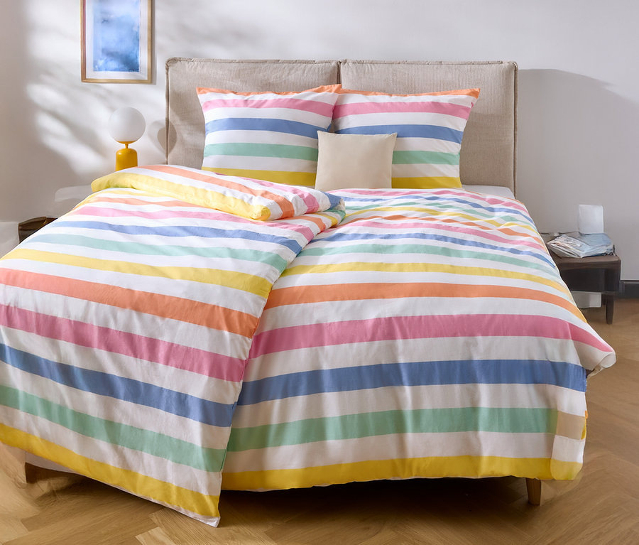 Bett mit bunt gestreifter Bettwäsche und zwei Kissen.