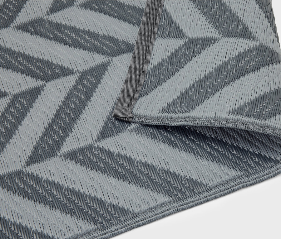 Eine graue Picknickdecke mit geometrischem Muster liegt gefaltet auf einem weißen Hintergrund.