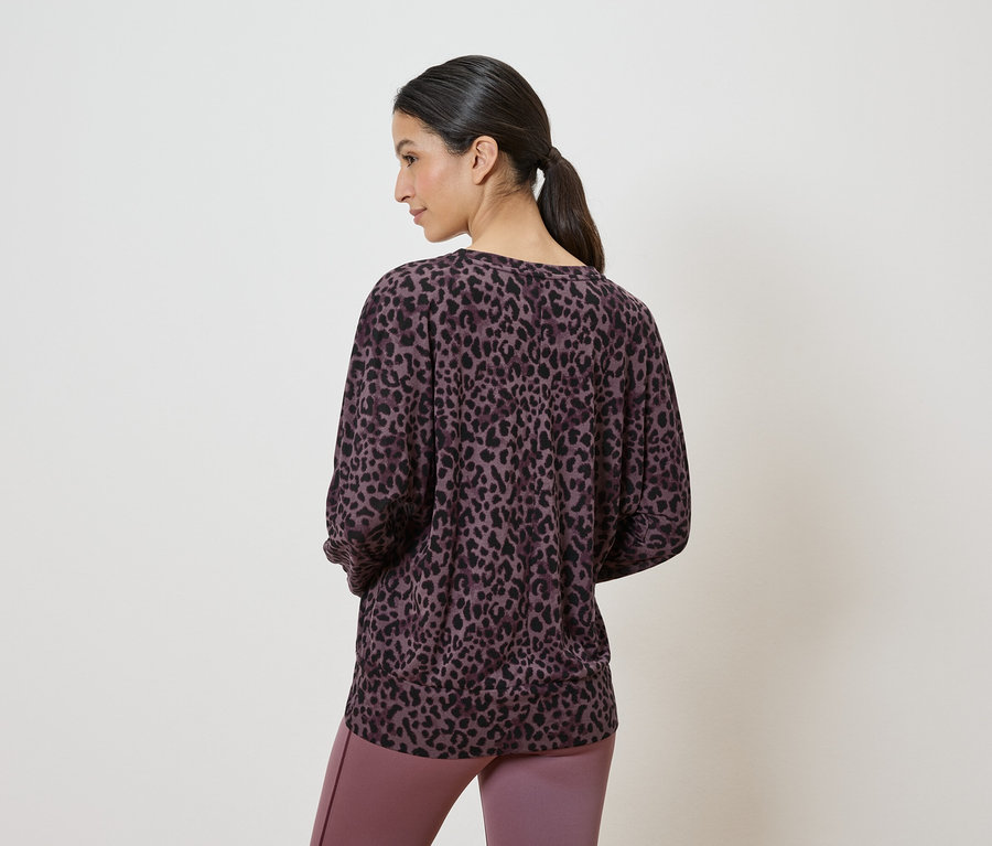 Frau von hinten, trägt einen lila-schwarzen Animal-Print Pullover und lila Leggings.