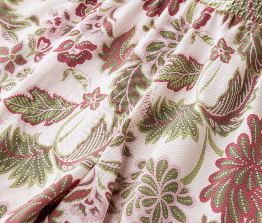 Nahaufnahme eines Stoffes mit Blätter- und Blumenmuster in Grün- und Rottönen.