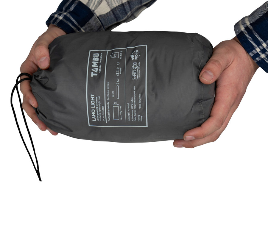 Person hält einen grauen Packsack mit der Aufschrift TAMBU LANO LIGHT Isomatte.