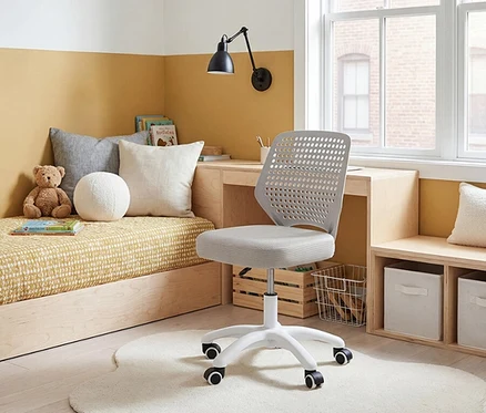 Ein Kinderzimmer mit einem Bettsofa, einem Schreibtisch mit Lampe und einem grauen Bürostuhl auf einem weißen Teppich.