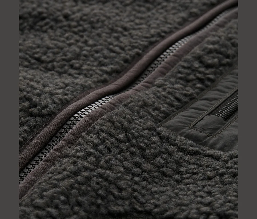 Nahaufnahme einer dunkelgrauen Fleecejacke mit teilweise geöffnetem Reißverschluss und einer Reißverschlusstasche rechts.