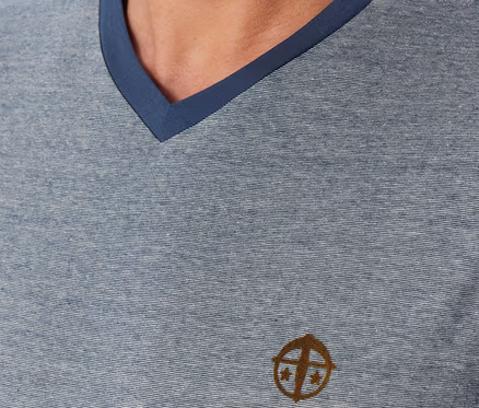 Nahaufnahme eines Mannes in einem blau-grau melierten V-Ausschnitt-Shirt mit dunkelblauem Kragen und einem braunen Logo auf der Brust.